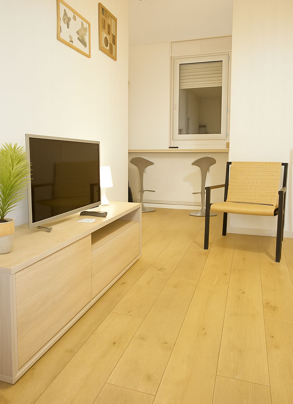 Un salon moderne avec un tél éviseur à écran plat, une petite table avec une lampe, un fauteuil et une fenêtre avec des stores.