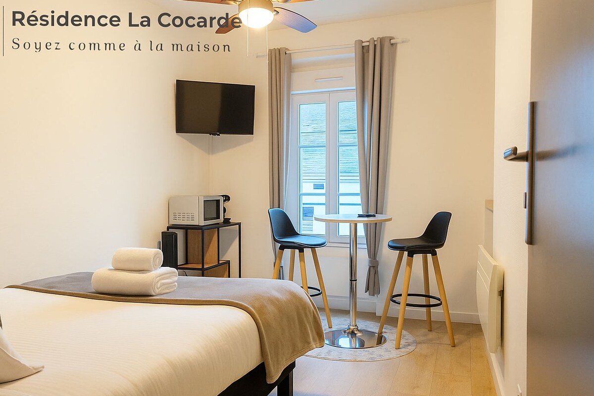 A hotel room with a bed, a TV, a microwave, two chairs, and a small table.