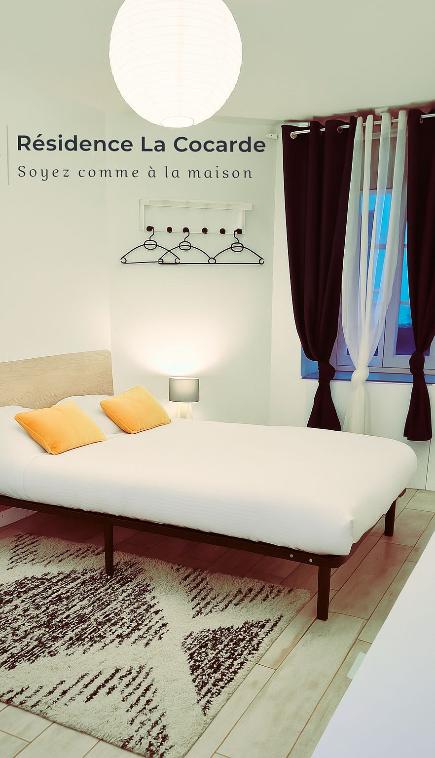 Ein modernes Schlafzimmer mit Bett, einem Wandhaken für Kleidung, einer Nachttischlampe und einem Fenster mit Vorhängen.