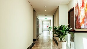 A hotel corridor with a marble floor, potted plants, and framed pictures on the walls. - Phu Thang Grand Hotel (Duc Hoa)