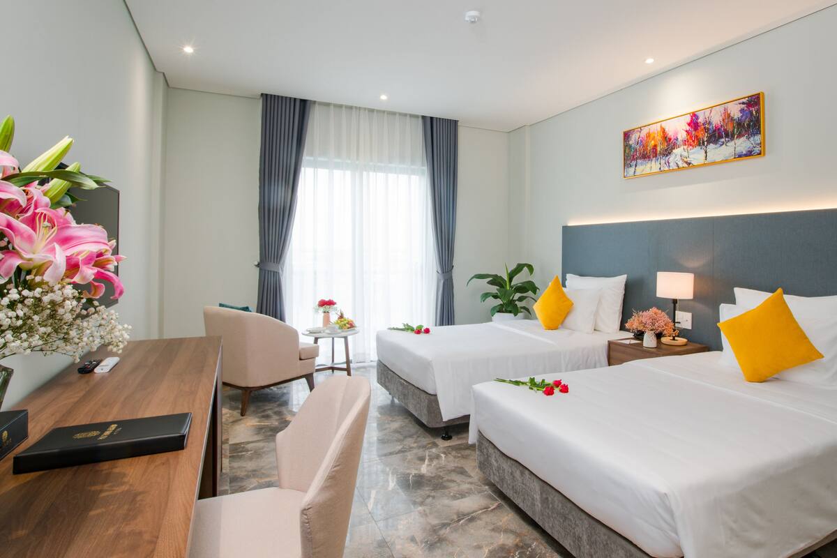 Hotelkamer met twee bedden, een bureau, een stoel, een kleine tafel met bloemen en een schilderij aan de muur.