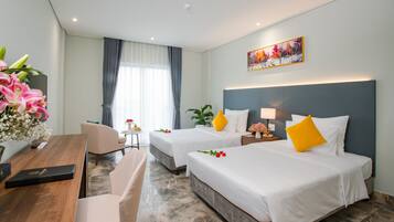 Habitación de hotel con dos camas, un escritorio, una silla, una mesita con flores y un cuadro en la pared.