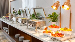 A buffet setup with multiple serving stations, a potted plant, and a lamp. - Phu Thang Grand Hotel (Duc Hoa)