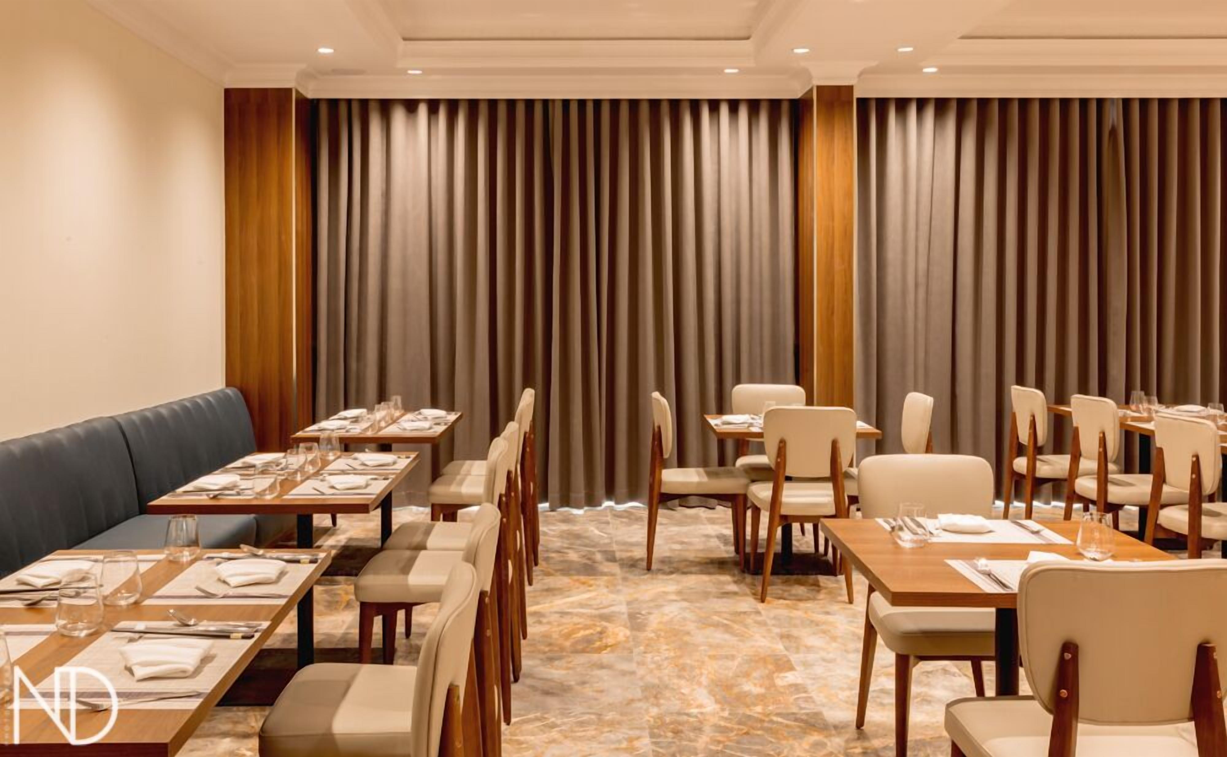 A hotel dining area with multiple tables and chairs, a sofa, and a large curtain backdrop.
