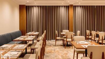 A hotel dining area with multiple tables and chairs, a sofa, and a large curtain backdrop.