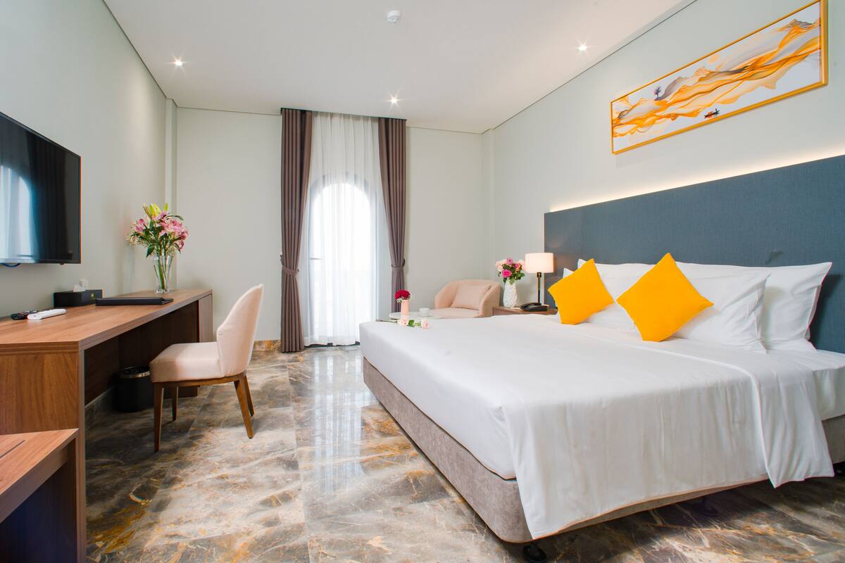 Een hotelkamer met een bed, een bureau, een stoel, een televisie en een schilderij aan de muur.