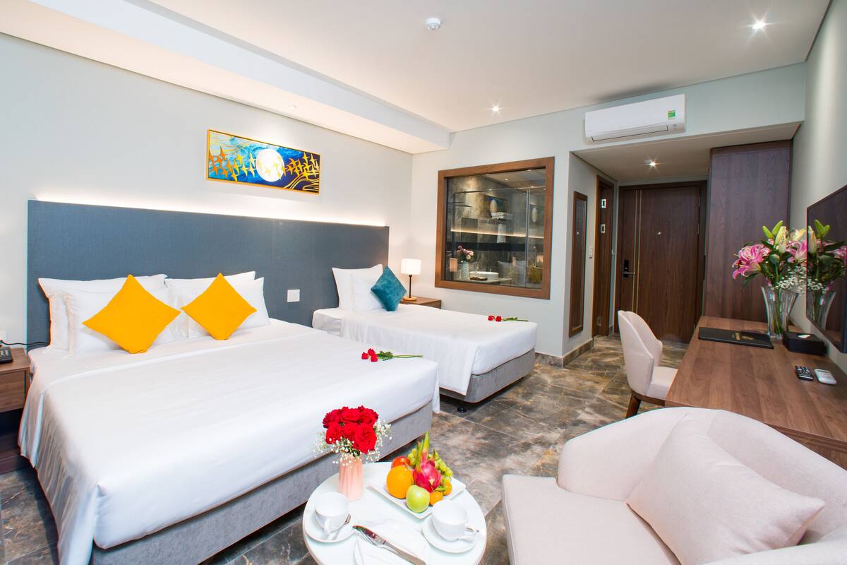 Een hotelkamer met twee bedden, een bureau, een stoel en een badkamer zichtbaar door een glazen deur.