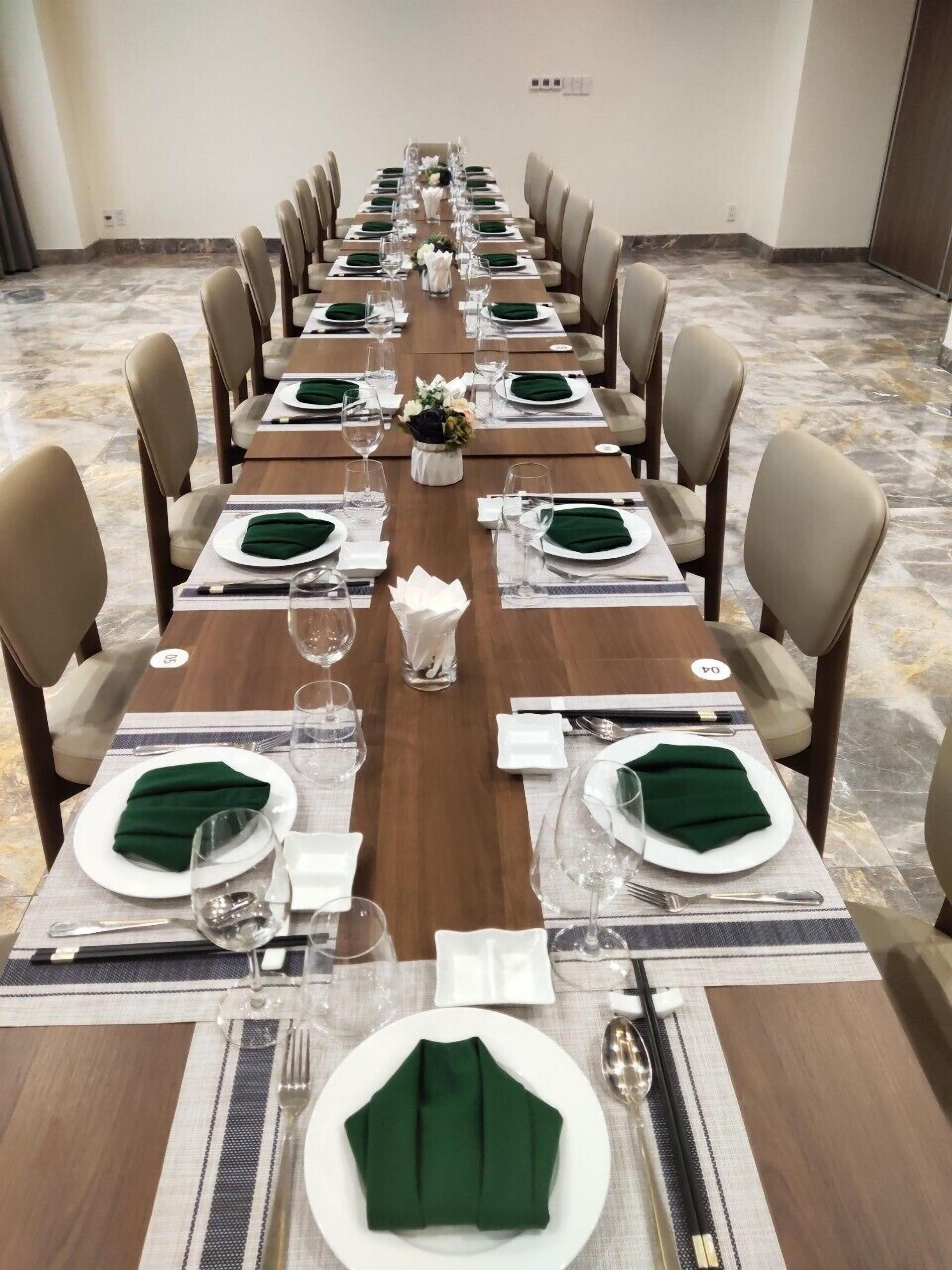 Een lange vergader tafel gedekt voor een formeel evenement, met stoelen, servies en een bloemenvaas.