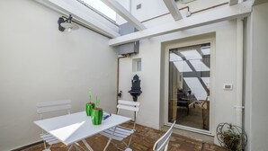 A patio with a white table and chairs, a small black wall-mounted light, and a door leading to an interior space. - Pimpotta House (Ravenna)
