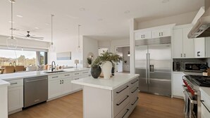 A modern kitchen with white cabinetry, stainless steel appliances, and a central island with a potted plant. - Breathtaking Wildfire Golf Views | Pool (Phoenix)