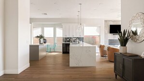 A modern kitchen with white cabinets, a marble island, and a dining area with a teal chair. - Breathtaking Wildfire Golf Views | Pool (Phoenix)