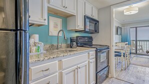 A kitchen with white cabinets, a stainless steel refrigerator, a microwave, and a coffee maker. - Turtle Cove, Spectacular Ocean Front 1 bedroom! (Myrtle Beach)
