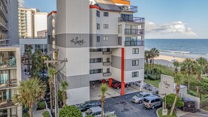 A multi-story hotel with balconies, a parking area, and a view of the beach. - Turtle Cove, Spectacular Ocean Front 1 bedroom! (Myrtle Beach)