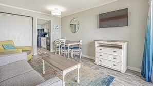 A living room with a sofa, coffee table, dining table, chairs, and a TV. - Turtle Cove, Spectacular Ocean Front 1 bedroom! (Myrtle Beach)