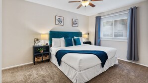 A bedroom with a bed, a nightstand, a ceiling fan, and a window with curtains. - East Side Oasis with Hot Tub (Loveland)