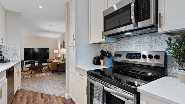 A modern kitchen with white cabinetry, a built-in microwave, a stove, and a dining area with a TV and a coffee machine. - East Side Oasis with Hot Tub (Loveland)