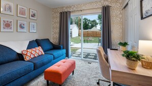 A living room with a blue sofa, a wooden coffee table, and a sliding glass door leading to a backyard. - East Side Oasis with Hot Tub (Loveland)