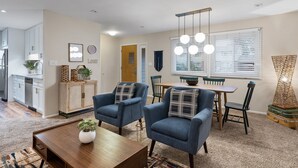 A modern living room with a dining area, featuring a kitchen in the background, a chandelier, and a decorative wall piece. - East Side Oasis with Hot Tub (Loveland)