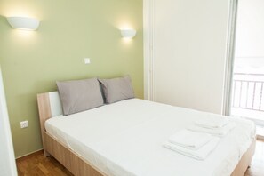 A neatly made bed with white bedding and two pillows, a wooden headboard, and two wall-mounted light fixtures.