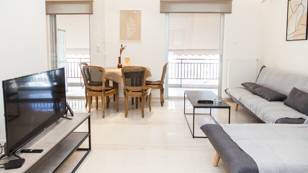 A modern living room with a flat-screen TV, a sofa, a coffee table, and a dining area with chairs and a table. - Gorgeous apartment in Central Athens (Athens)
