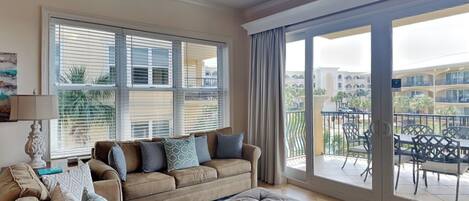 A spacious living room with a large window, a ceiling fan, and a view of a building and palm trees outside.