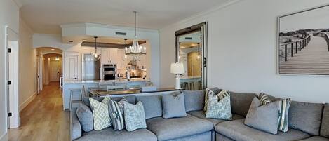 A modern living room with a grey sectional sofa, a dining area, and a kitchen in the background.