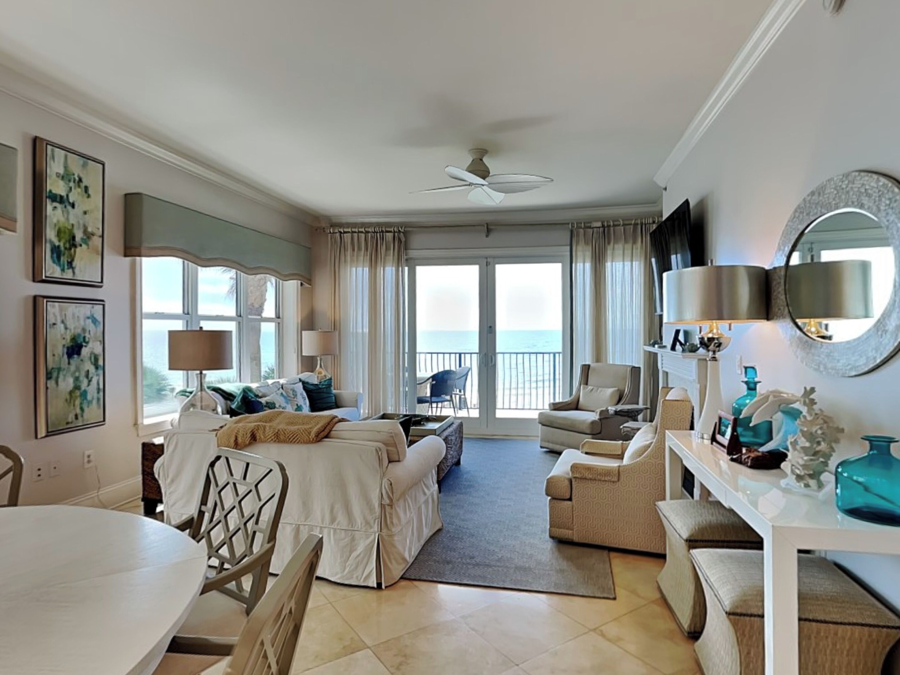 A spacious room with a bed, two armchairs, a dining table, and a view of the sea through large windows.