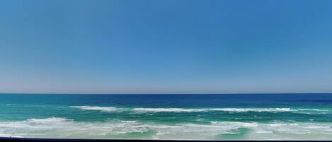 Vista da praia com grade, ondas do oceano e guarda-sóis.