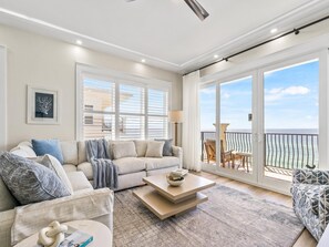 A spacious living room with a large window, a sofa, a coffee table, and a view of the ocean. - Adagio by Southern Vacation Rentals (Santa Rosa Beach)
