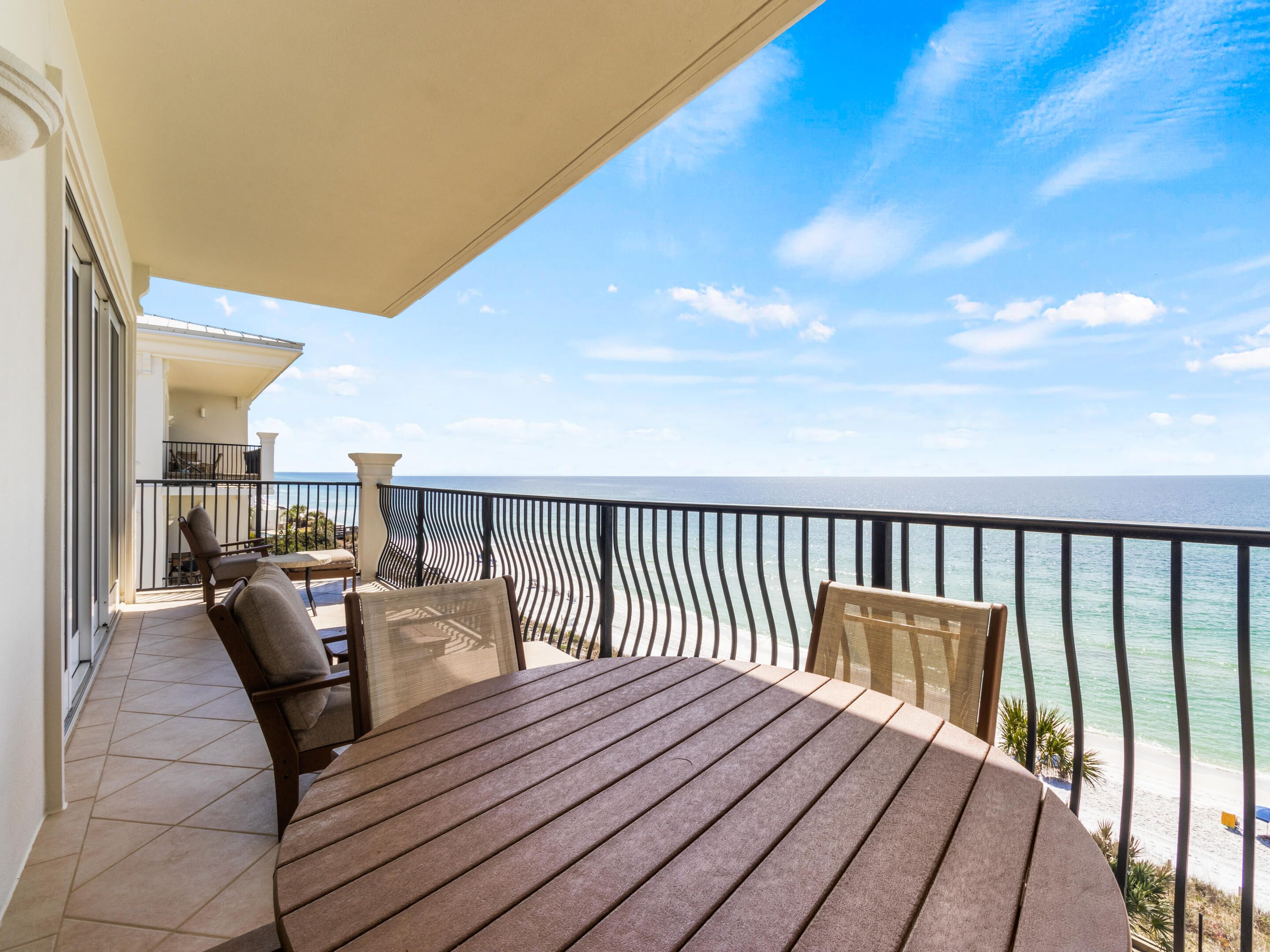 A balcony with a wooden table and chairs, overlooking a beach and the ocean.