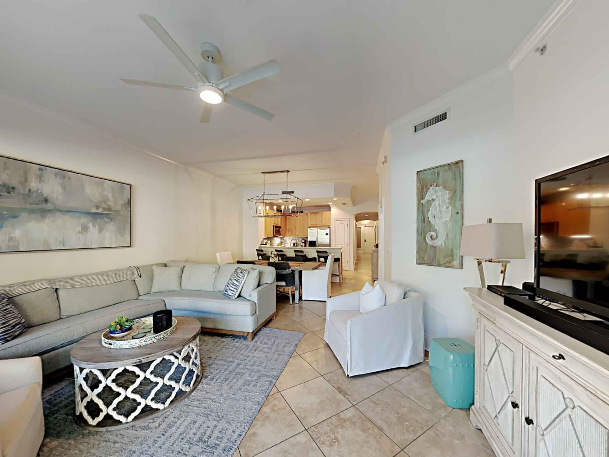 A modern living room with a sofa, coffee table, and TV stand. There is a kitchen in the background.