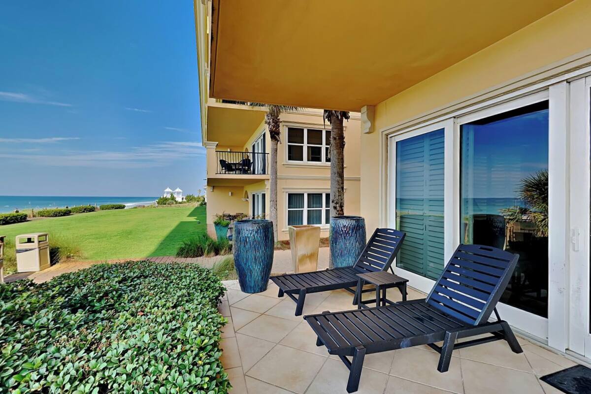 A balcony with two lounge chairs, a large vase, and a view of the ocean.