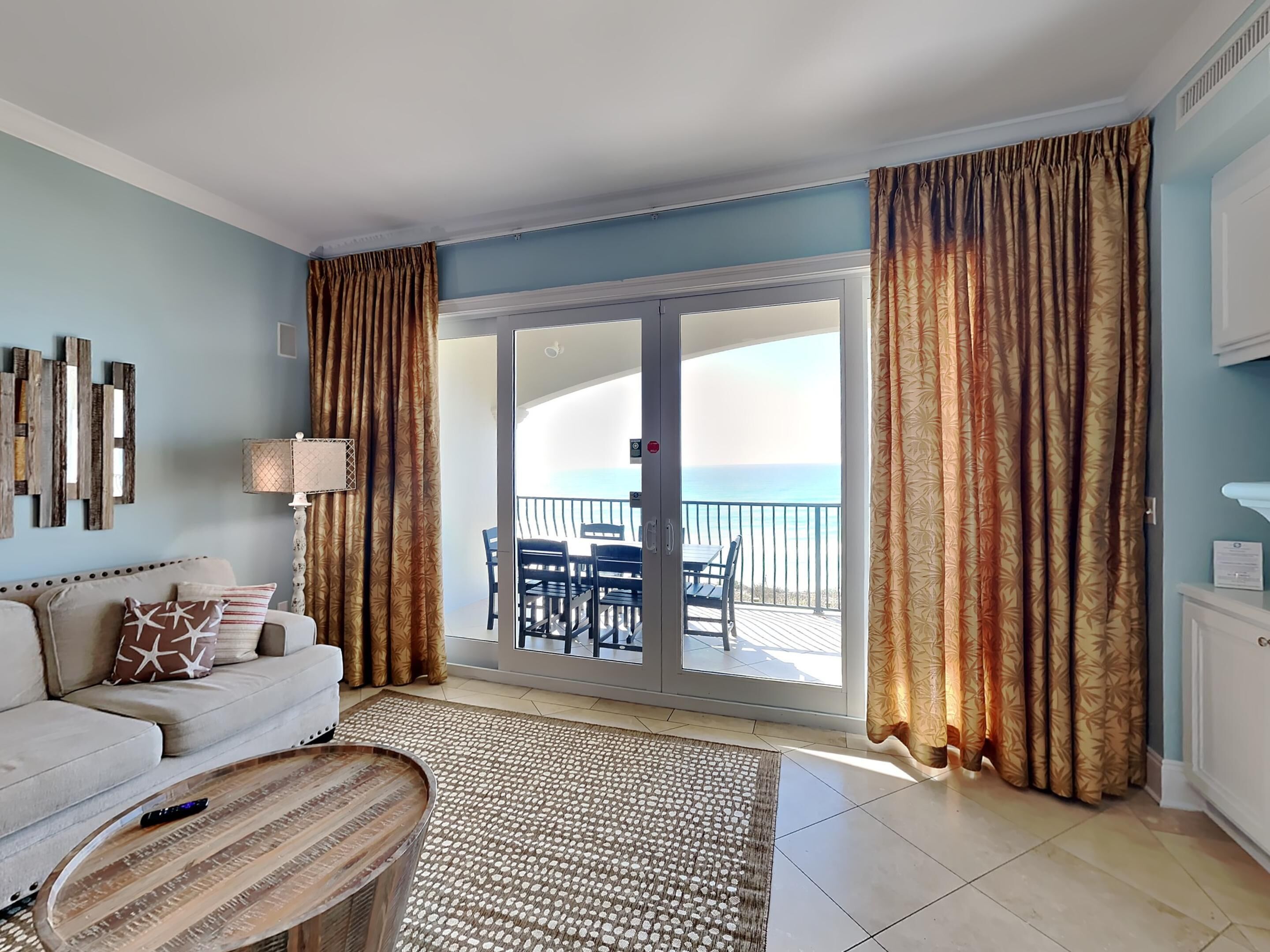 A living room with a sofa, a coffee table, and a view of the balcony with a table and chairs.