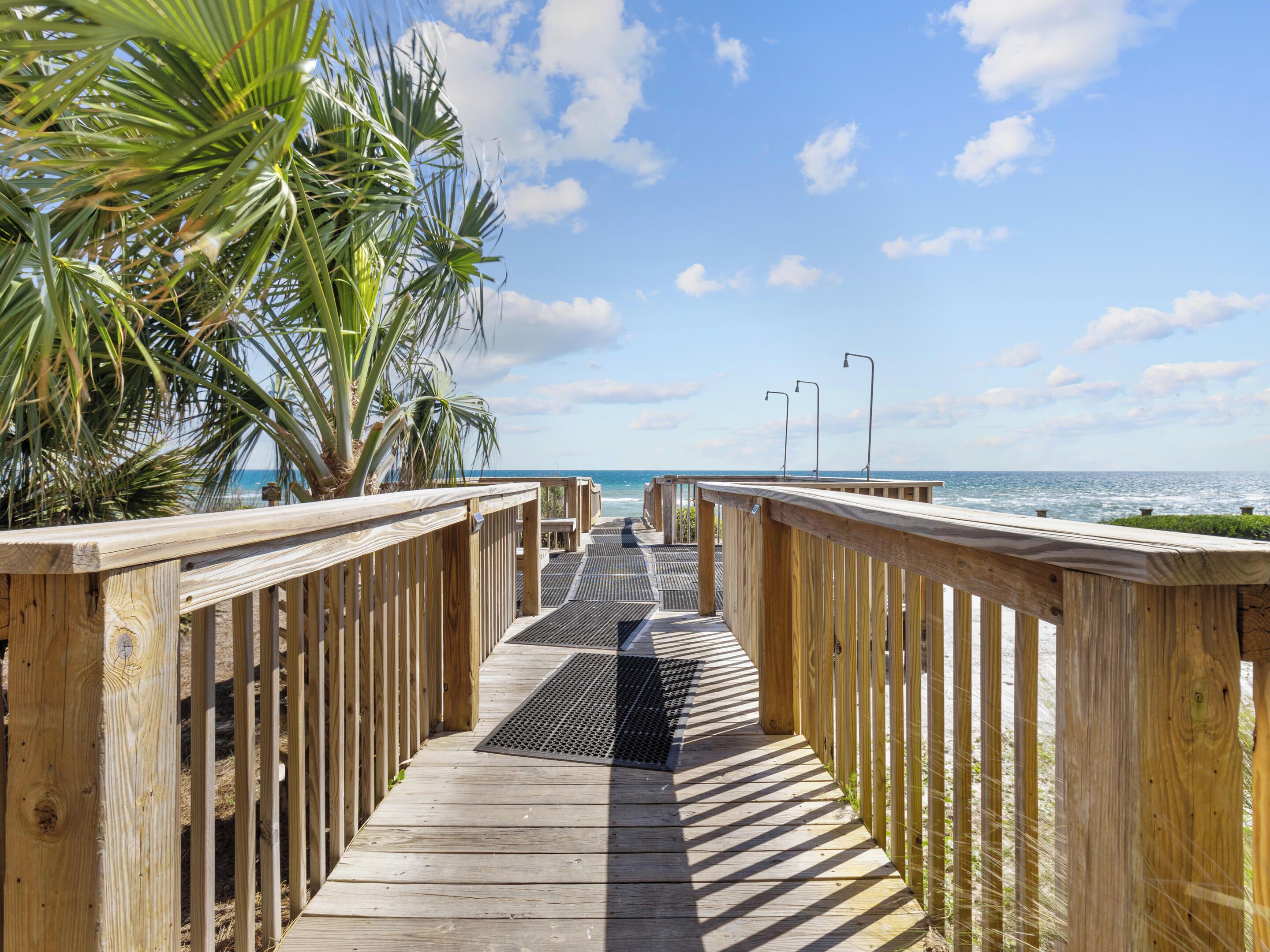 A wooden boardwalk leading to the beach with palm trees on one side.