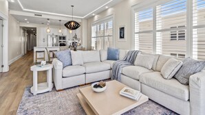A modern living room with a sectional sofa, a coffee table, and a dining area with a kitchen in the background. - Adagio by Southern Vacation Rentals (Santa Rosa Beach)