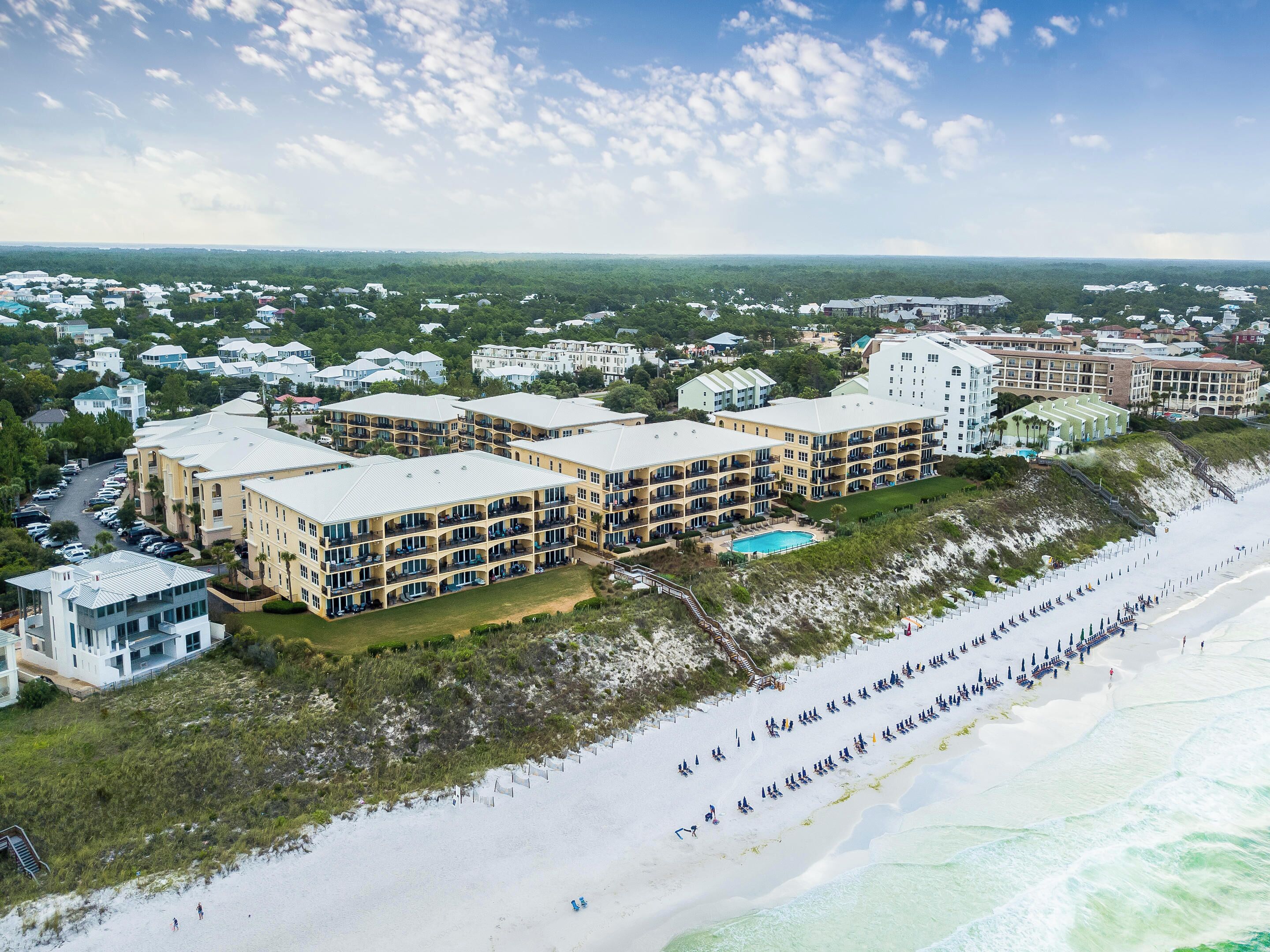 Un resort con varias construcciones, piscina y playa con sombrillas.