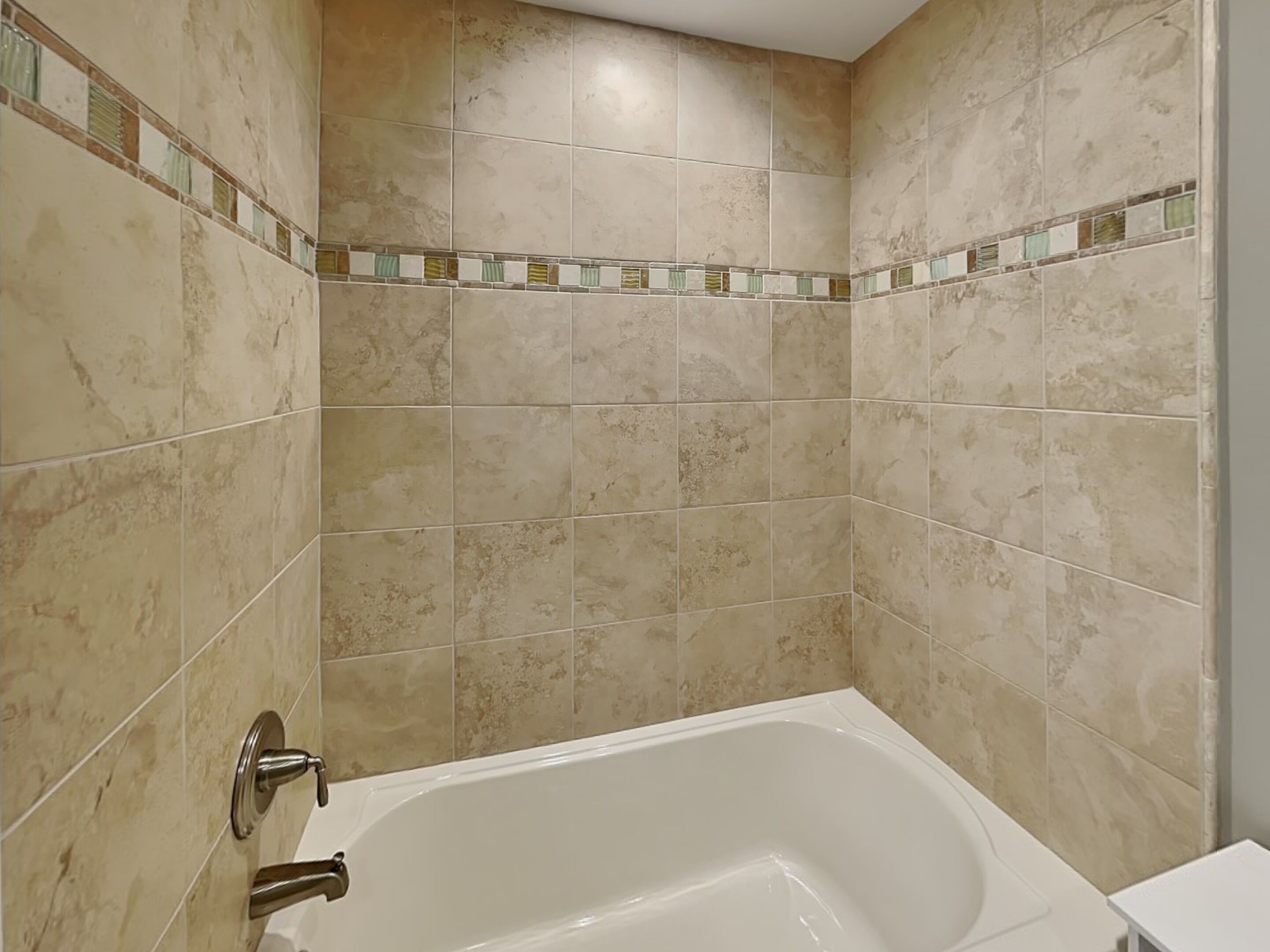 A bathroom with beige tiles, a white bathtub, and a shower area.