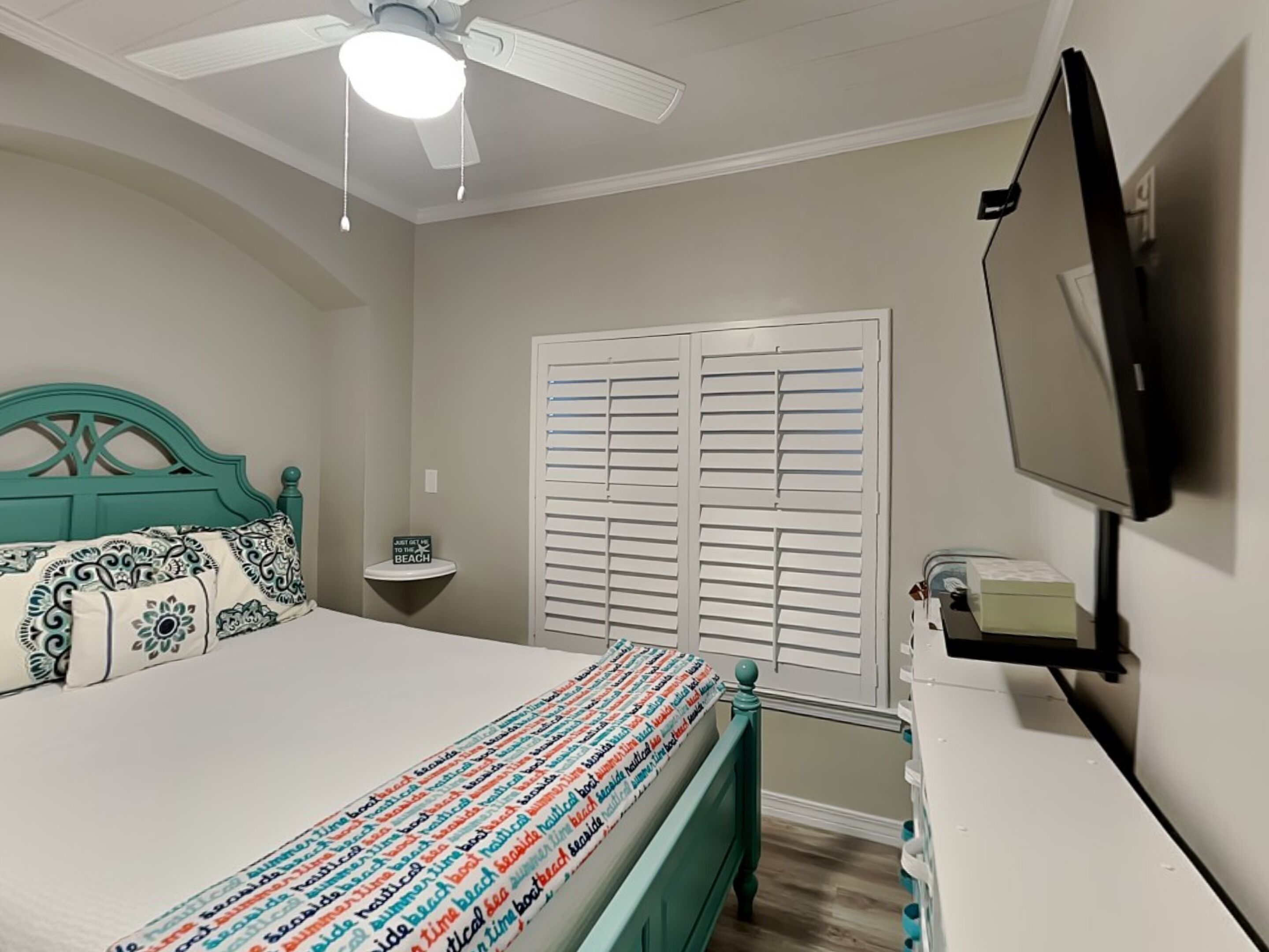 Ein Schlafzimmer mit einem Bett, einem Nachttisch, einem Fernseher und einem Deckenventilator.