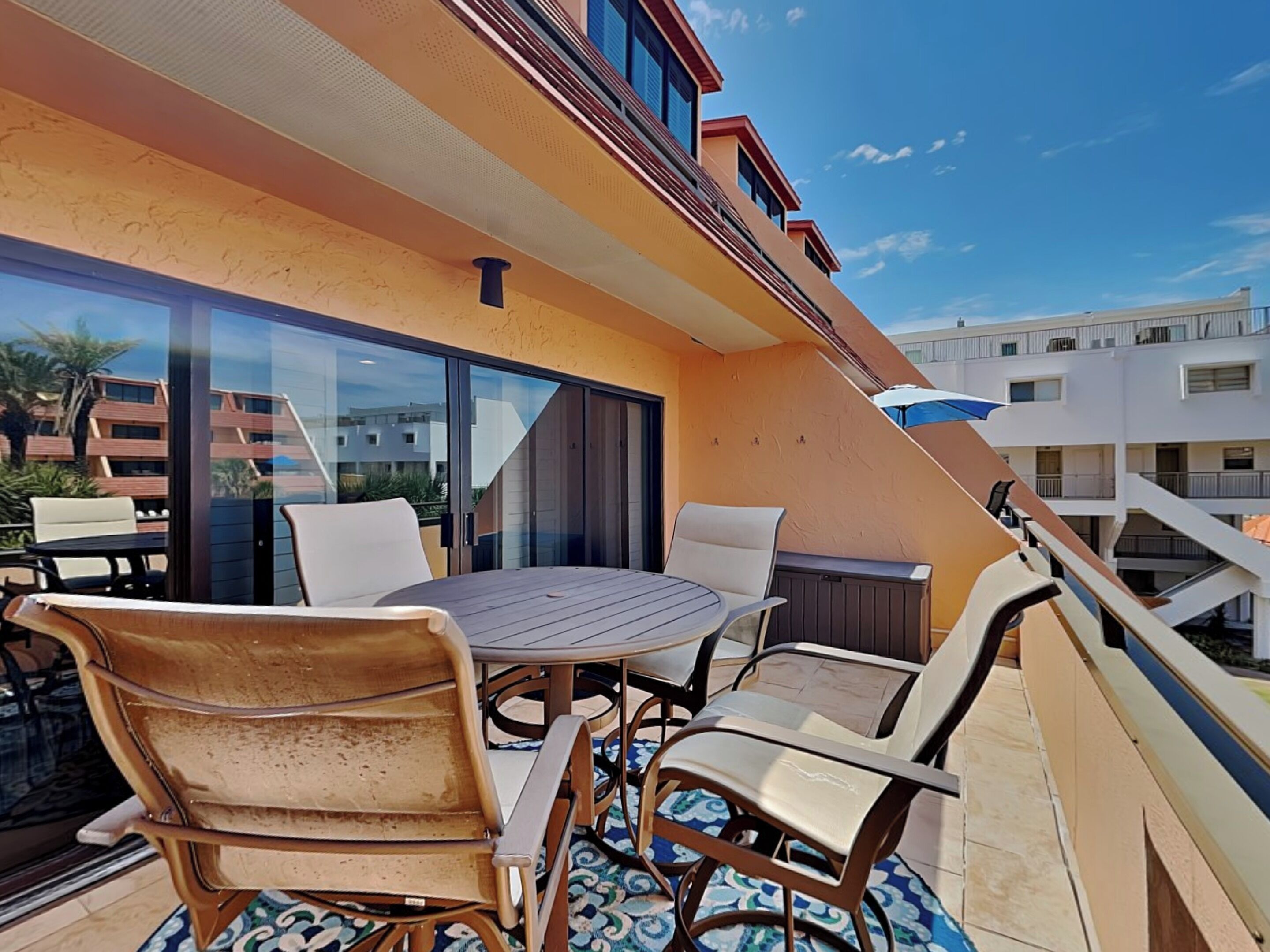 Un balcon avec une table ronde et des chaises, des portes vitrées et une vue sur d’autres immeubles.