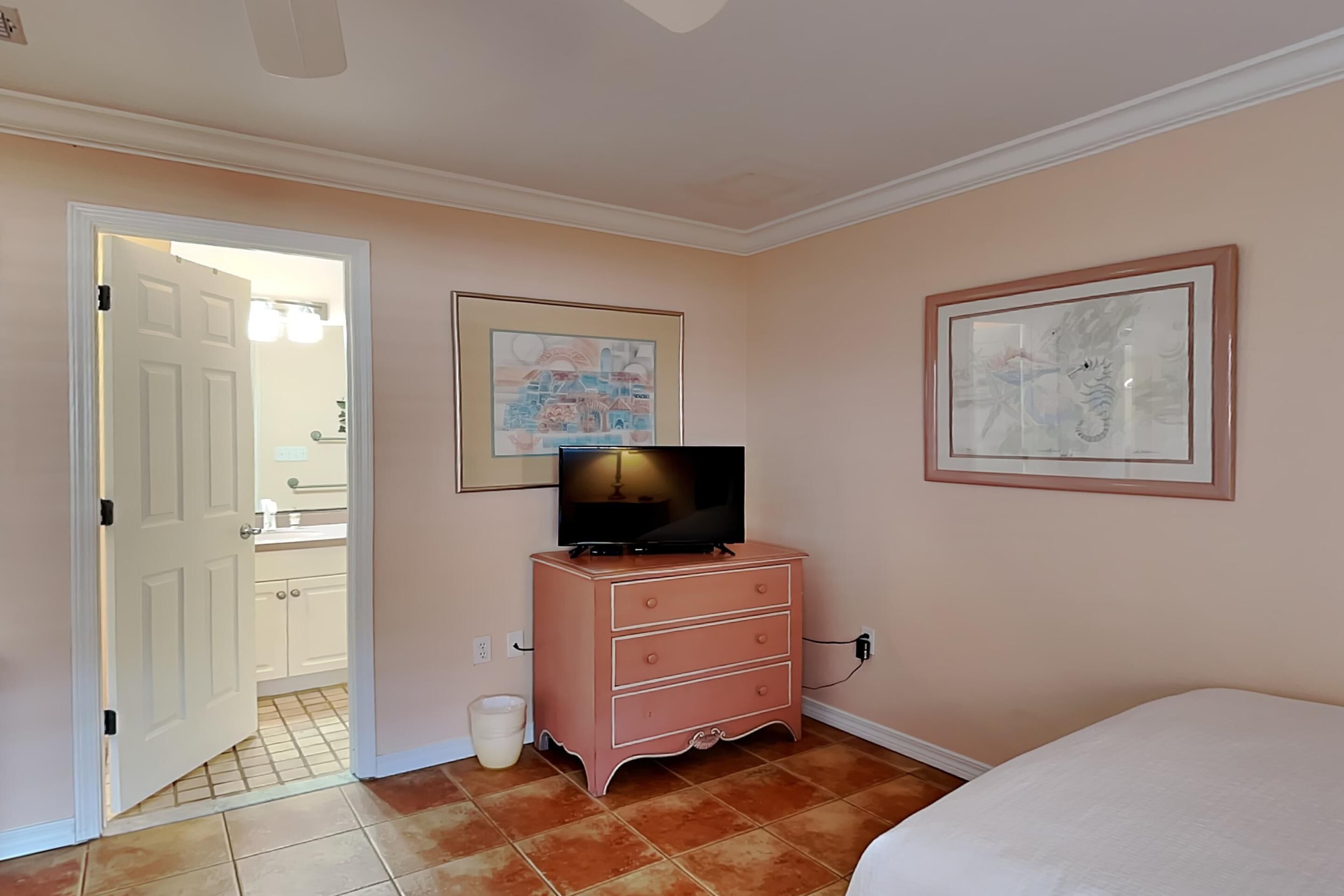 A bedroom with a bed, a pink dresser, a television, and two framed pictures on the wall.