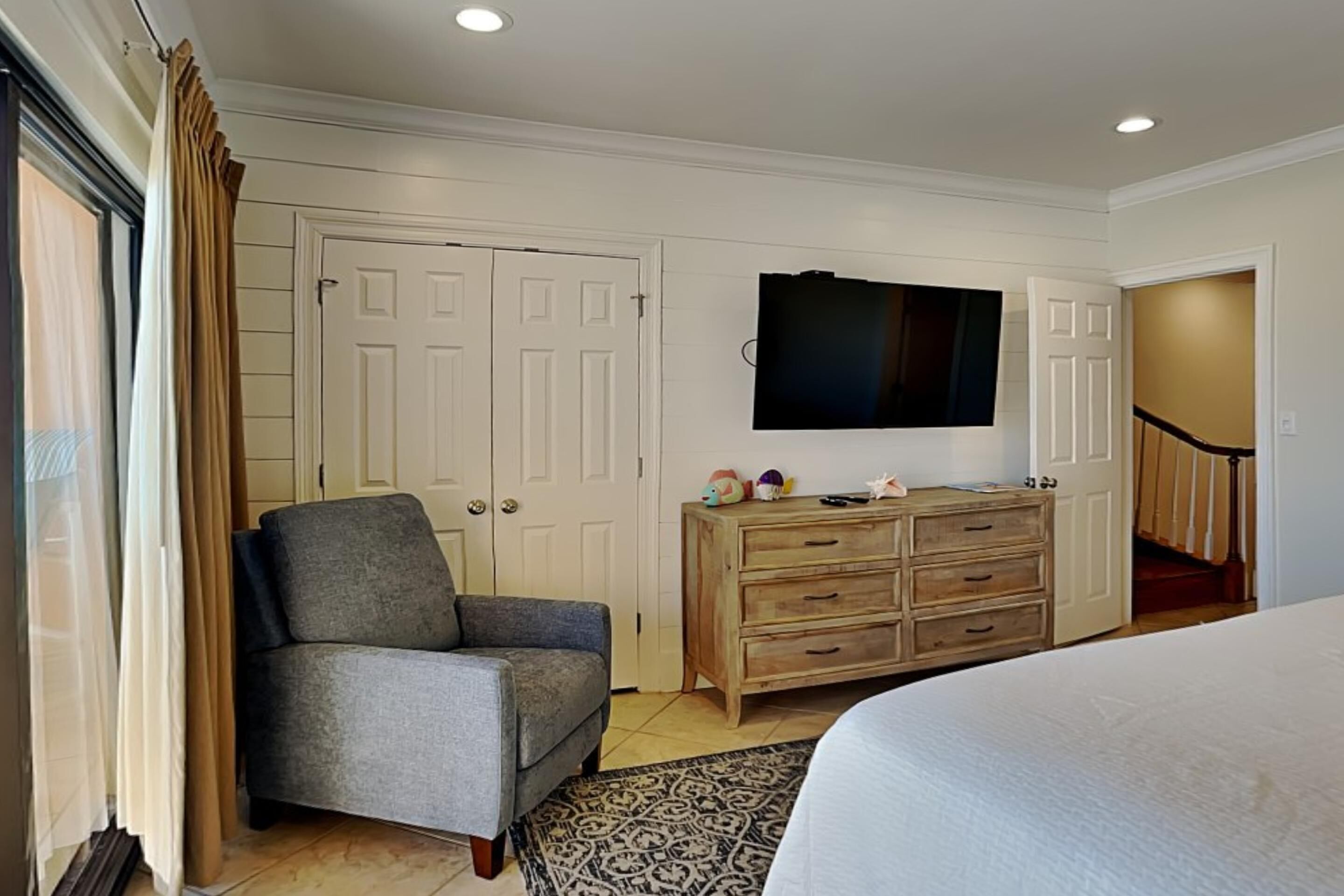 Un dormitorio con una cama, una silla, un tocador, un televisor y una escalera.