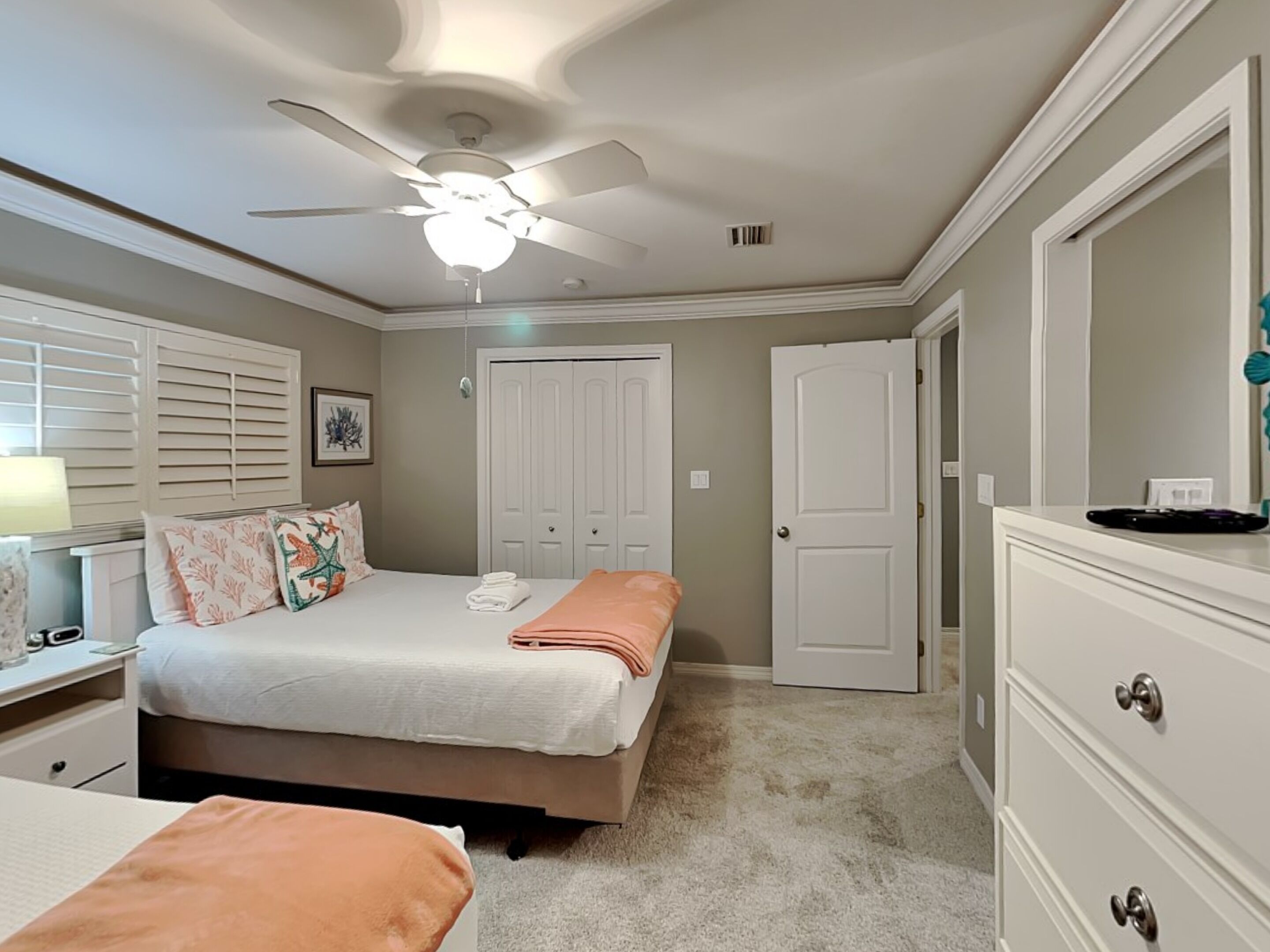 Un dormitorio con una cama, una mesita de noche, un aparador, un ventilador de techo y una puerta.
