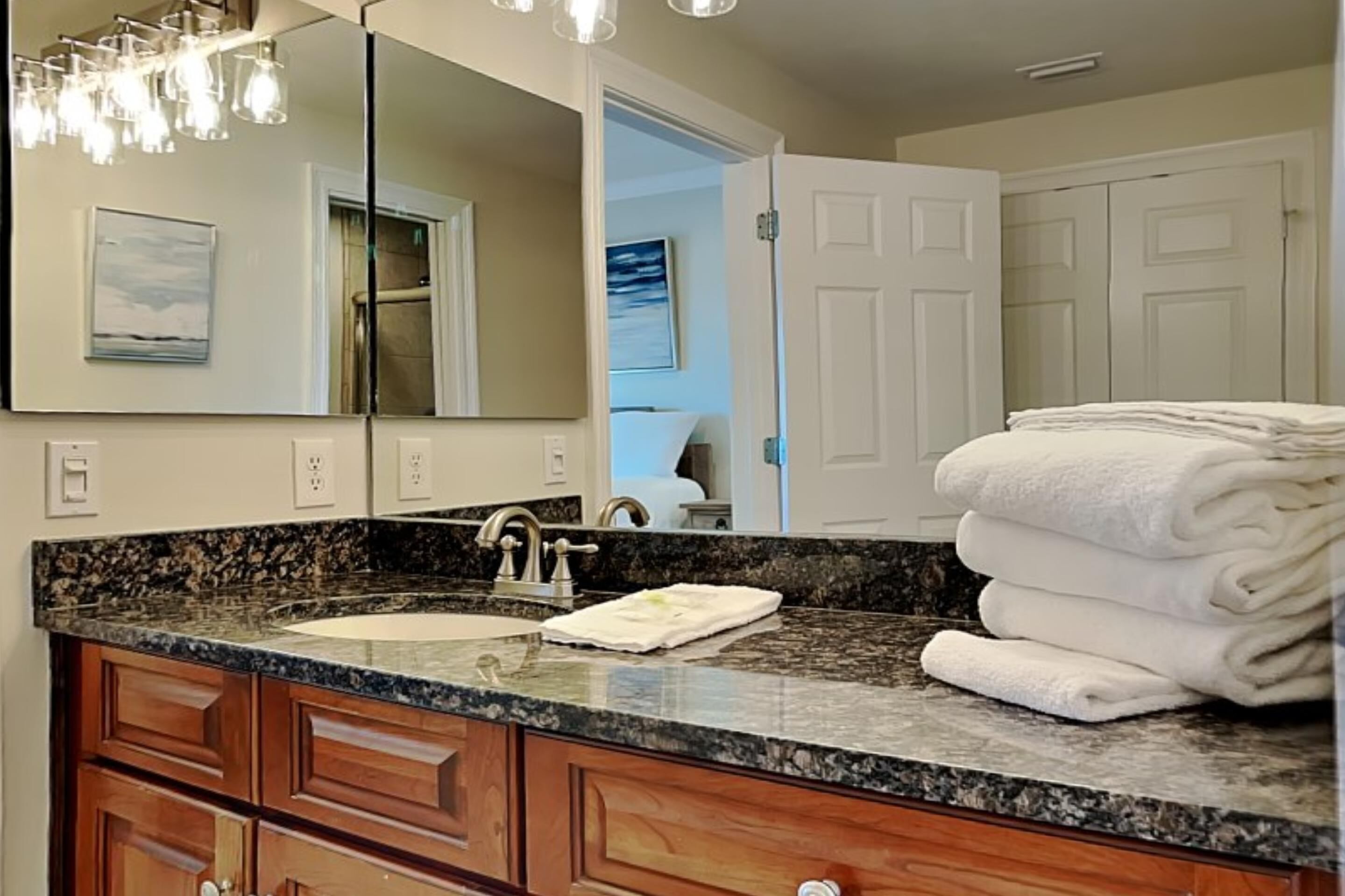 A bathroom with a granite countertop, a sink, a mirror, wooden cabinets, and a stack of white towels.