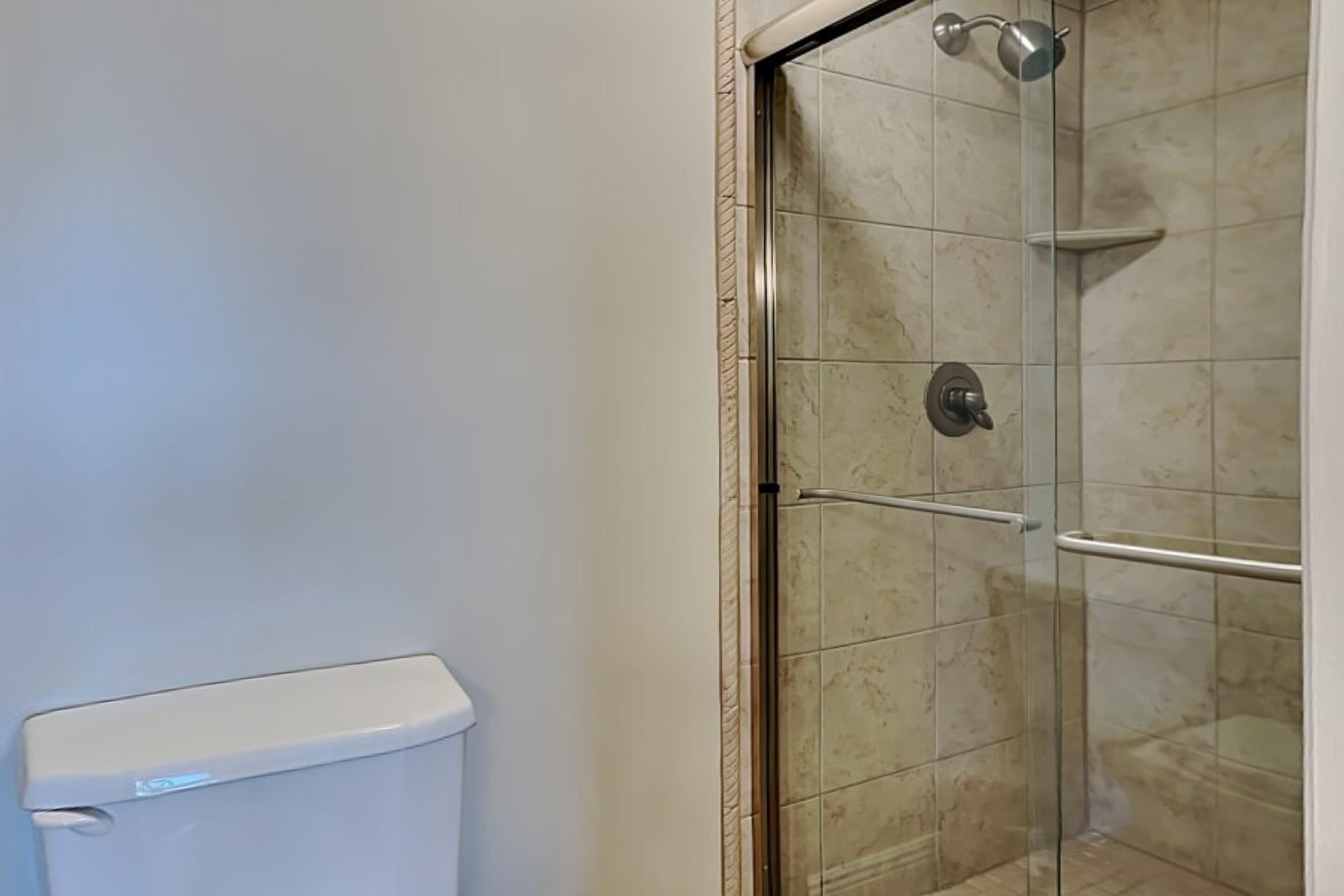 Une salle de bain équipée de toilettes, d’une douche à parois de verre et de murs carrelés.