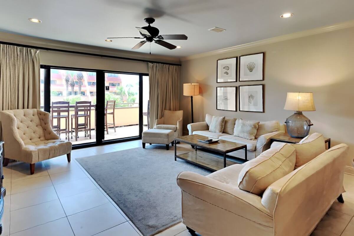 A spacious living room with a ceiling fan, a sofa set, a coffee table, and a view of the outside through a sliding glass door.