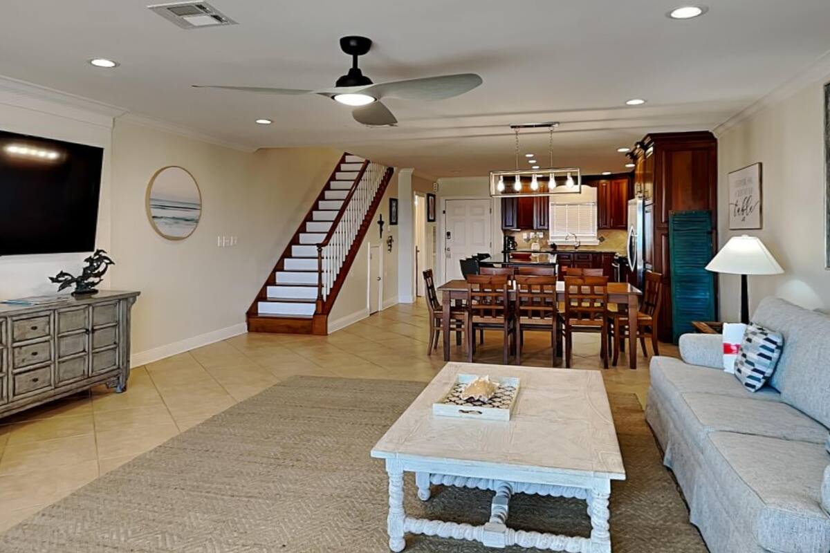 A spacious living room with a dining area, a staircase, and a kitchen in the background.