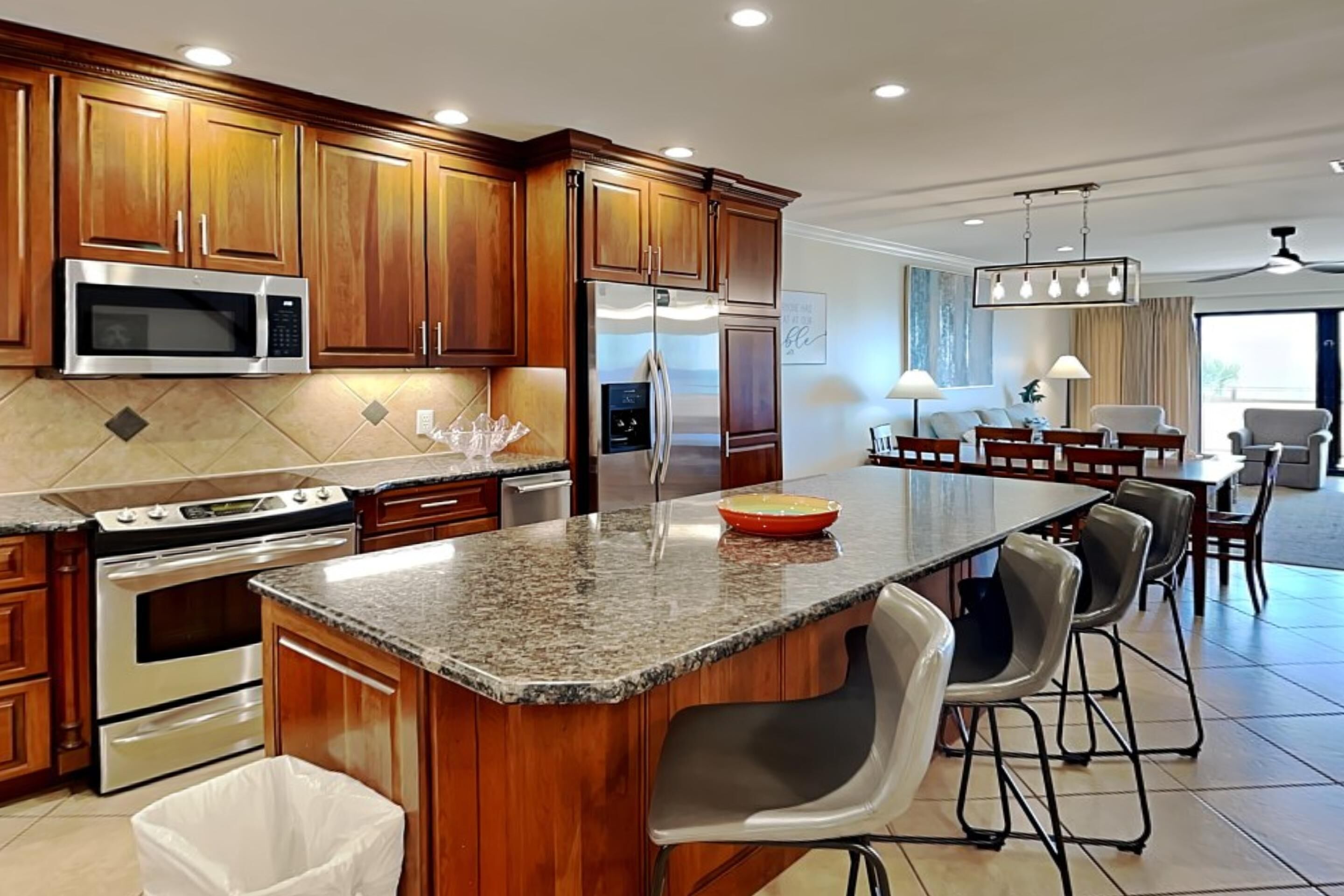 A modern kitchen with wooden cabinets, stainless steel appliances, granite countertops, and bar stools.
