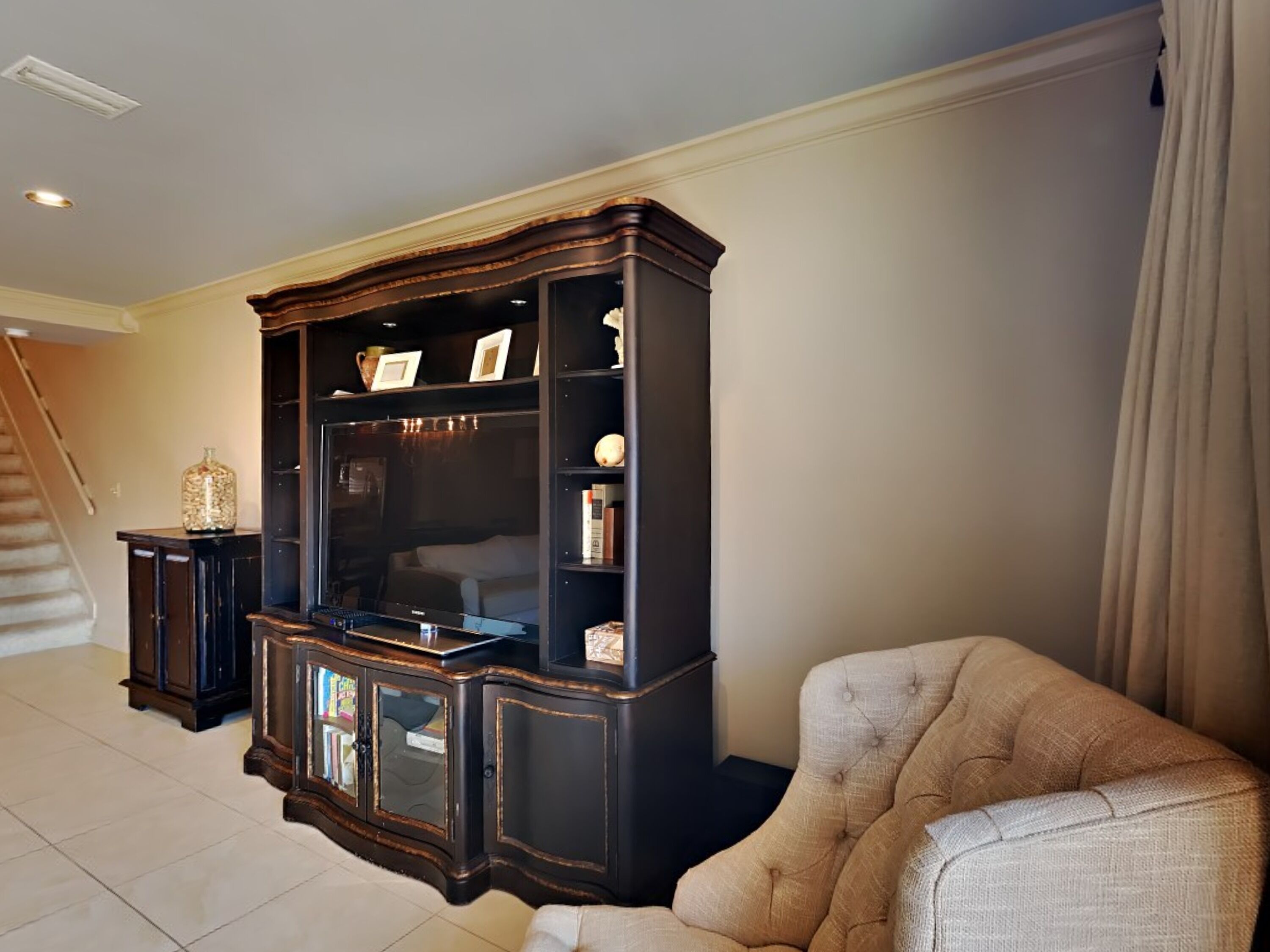 A living room with a dark wooden entertainment center, a beige armchair, and a staircase in the background.