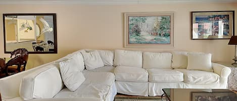 En stue med en hvid modulsofa, et sofabord og et gulvtæppe. Malerier hænger på væggene, og der er et spejl over sofaen.