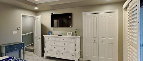 A bedroom with a bed, dresser, wardrobe, ceiling fan, and a mounted TV.